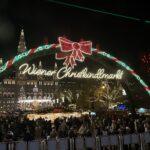 Crowds gather under a glowing arch labeled “Wiener Christkindlmarkt” at Vienna’s Christmas market.