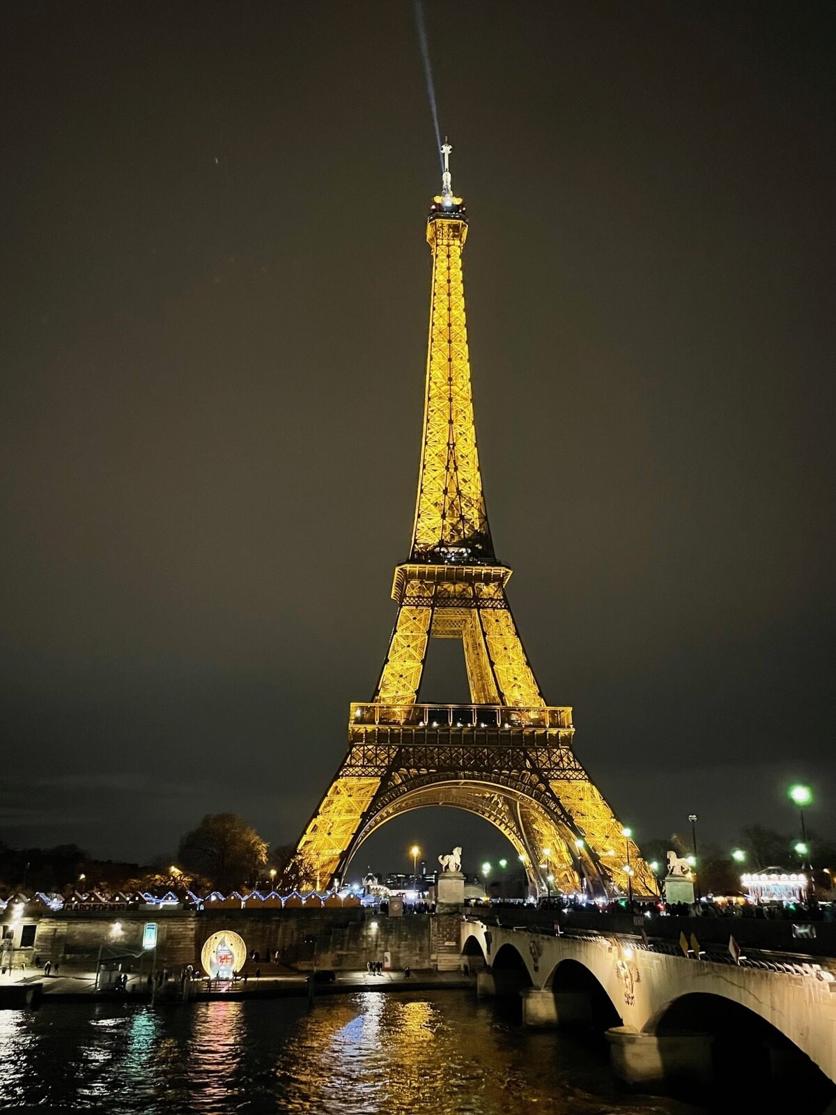 Eiffel Tower illuminated at night with reflections on the Seine River in Paris.